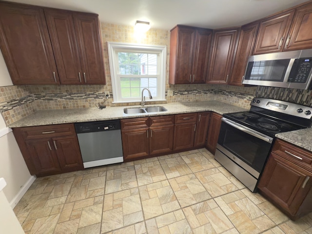 kitchen with a sink, appliances with stainless steel finishes, stone finish floor, and backsplash