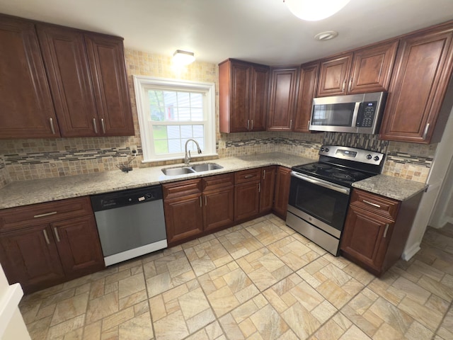 kitchen featuring stainless steel appliances, stone finish flooring, a sink, and tasteful backsplash