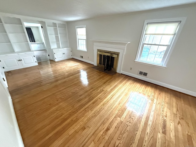unfurnished living room with visible vents, built in features, baseboards, light wood-type flooring, and a fireplace with flush hearth