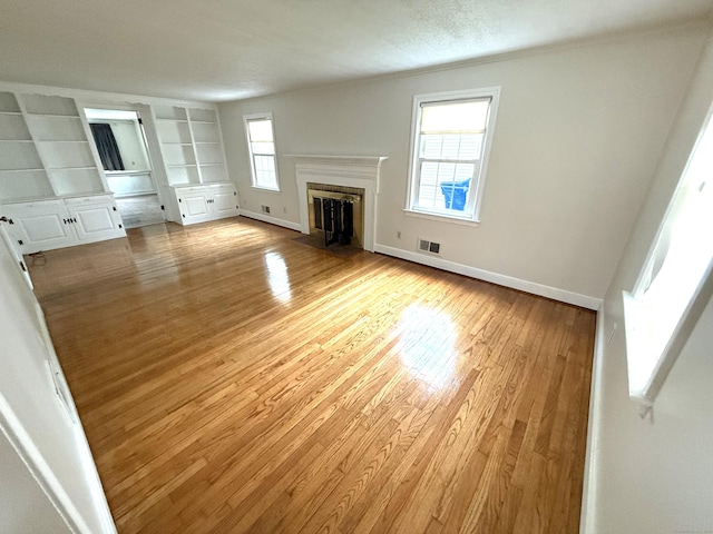 unfurnished living room with visible vents, a fireplace with flush hearth, built in features, baseboards, and light wood-style flooring