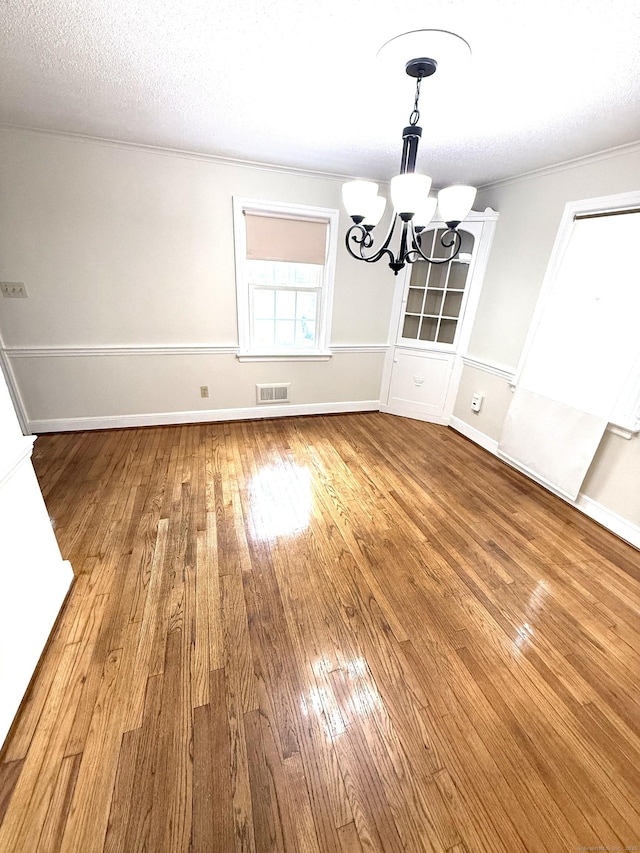 unfurnished dining area featuring visible vents, hardwood / wood-style flooring, baseboards, an inviting chandelier, and ornamental molding