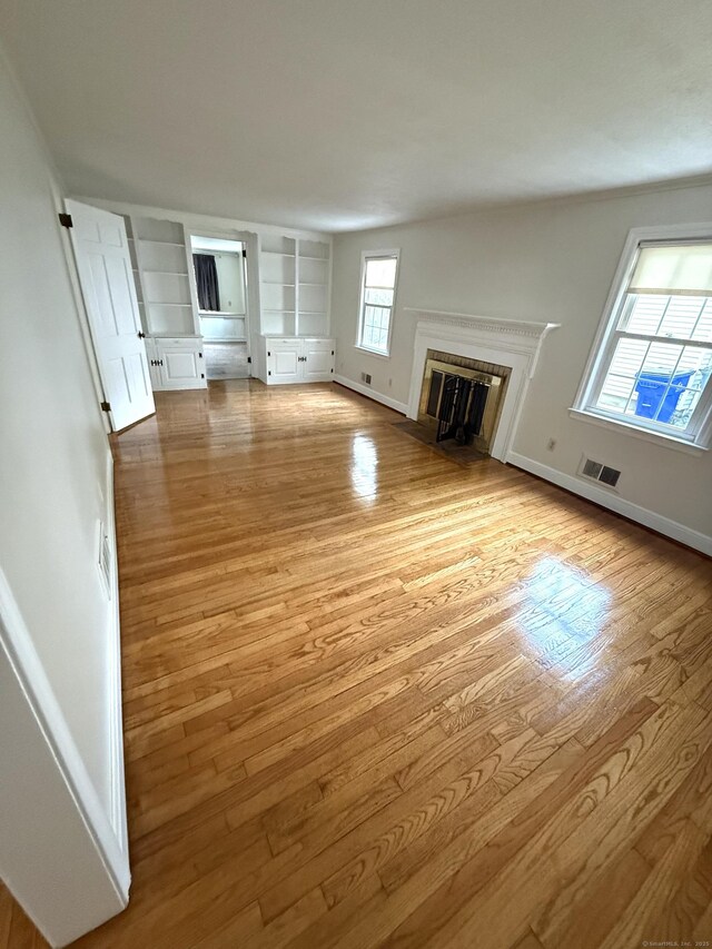 unfurnished living room featuring baseboards, a fireplace with flush hearth, light wood finished floors, and visible vents