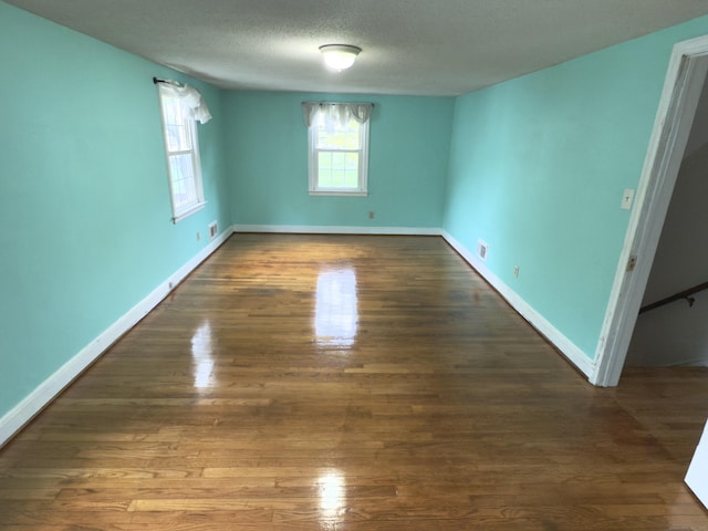 unfurnished room featuring baseboards, a textured ceiling, wood finished floors, and visible vents