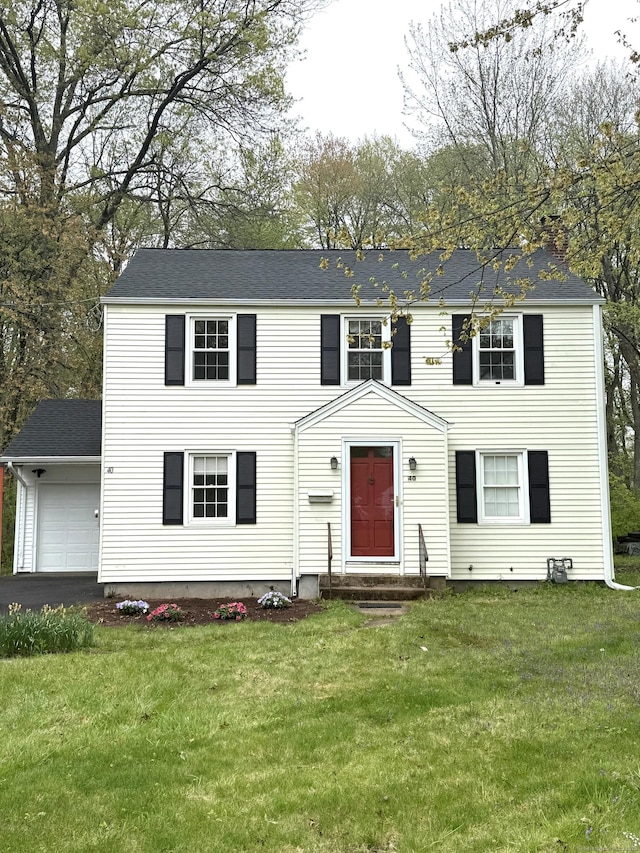 colonial home with a garage, a shingled roof, and a front lawn