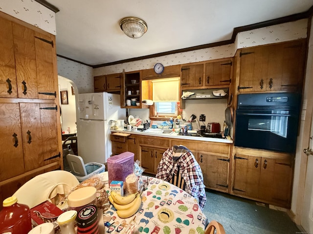 kitchen with brown cabinets, crown molding, black oven, freestanding refrigerator, and wallpapered walls