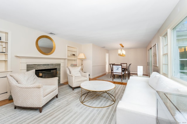 living area featuring a stone fireplace, visible vents, baseboards, light wood finished floors, and a chandelier