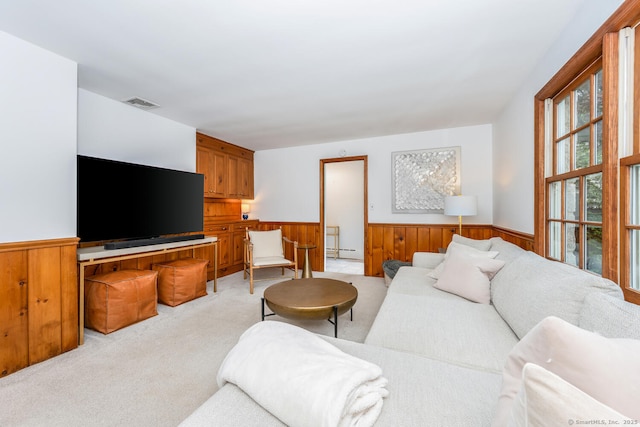 living area with visible vents, wainscoting, and light carpet