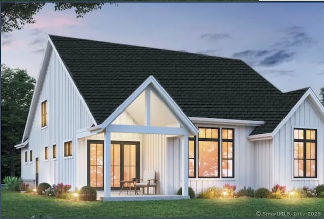 back of property with board and batten siding, a lawn, and roof with shingles