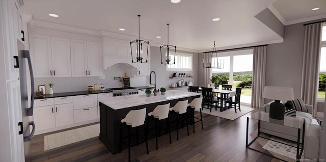 kitchen featuring stove, a center island with sink, dark wood-type flooring, tasteful backsplash, and a sink