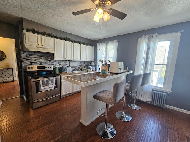 kitchen with dark wood-style flooring, electric range, a textured ceiling, radiator, and a kitchen bar