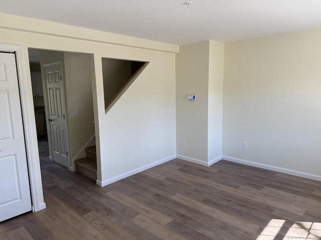 unfurnished room featuring dark wood-style flooring, baseboards, and stairway