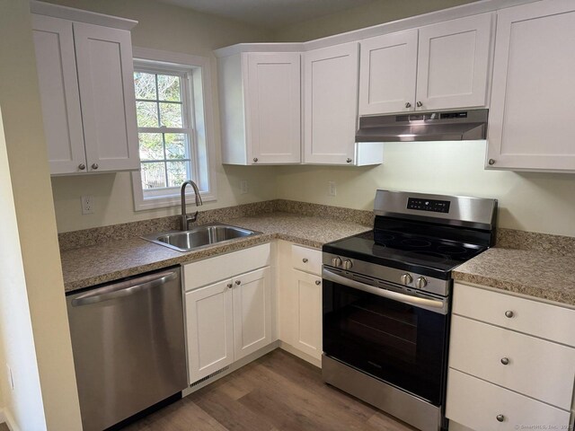 kitchen with white cabinets, appliances with stainless steel finishes, a sink, under cabinet range hood, and dark wood-style floors