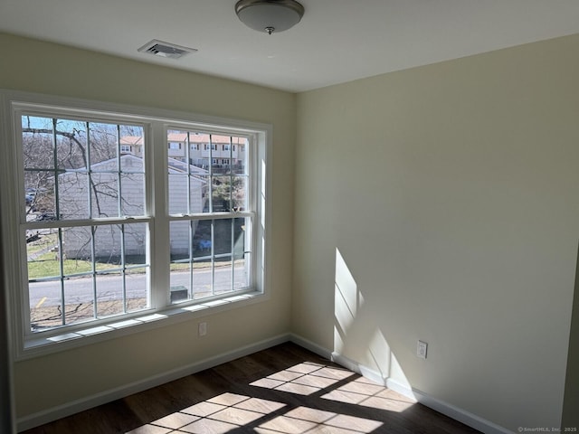 spare room featuring baseboards, visible vents, wood finished floors, and a wealth of natural light