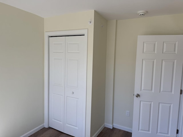 unfurnished bedroom featuring baseboards, dark wood-style flooring, and a closet