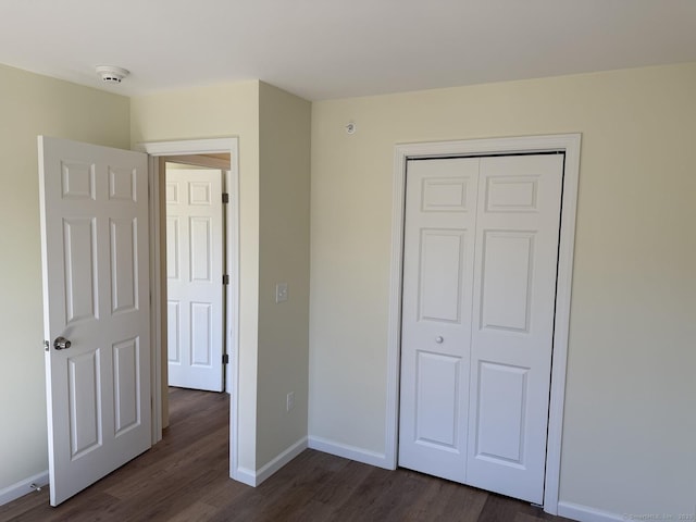 unfurnished bedroom with baseboards, a closet, and dark wood-style flooring