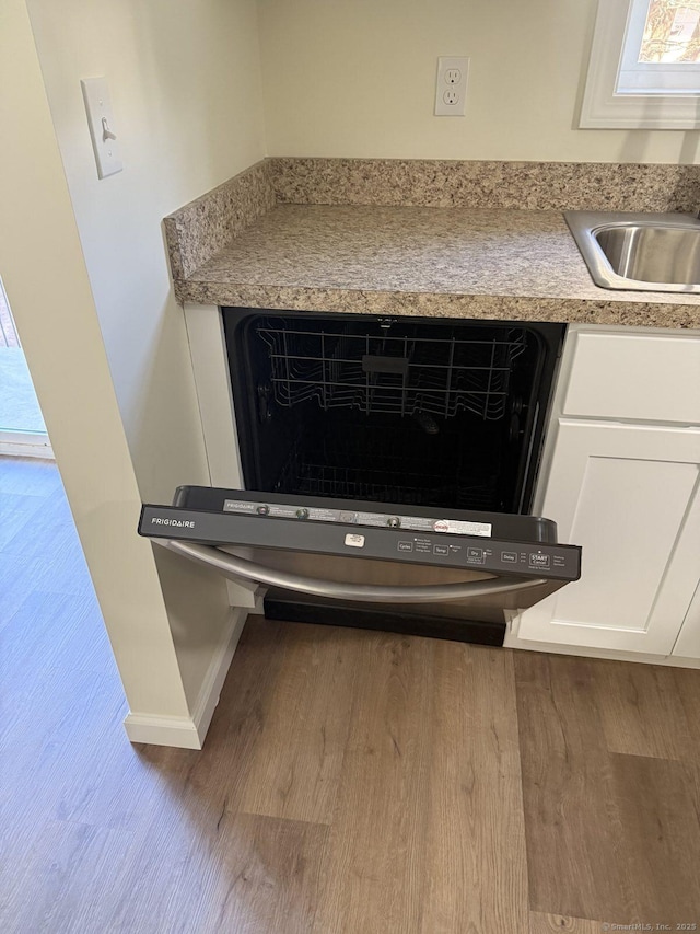 interior details featuring wood finished floors, a sink, baseboards, white cabinets, and dishwashing machine