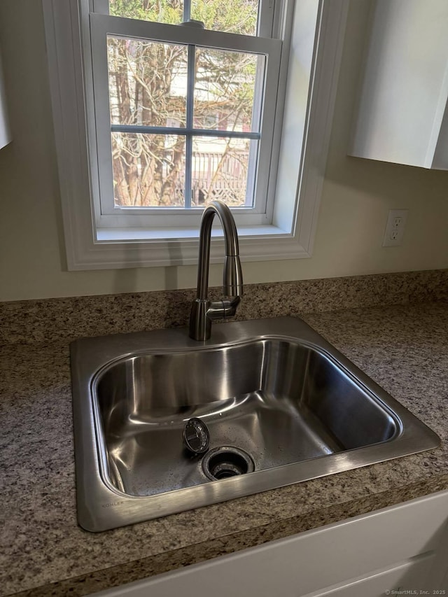 room details with a sink, white cabinets, and light stone countertops