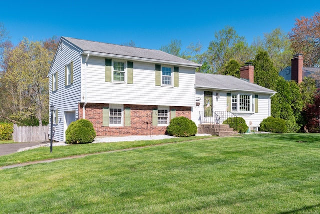 tri-level home featuring brick siding, a chimney, fence, and a front yard