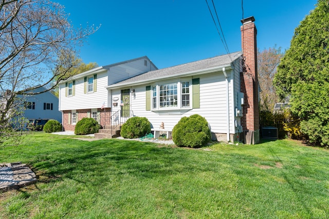 split level home with brick siding, a front yard, a chimney, and cooling unit