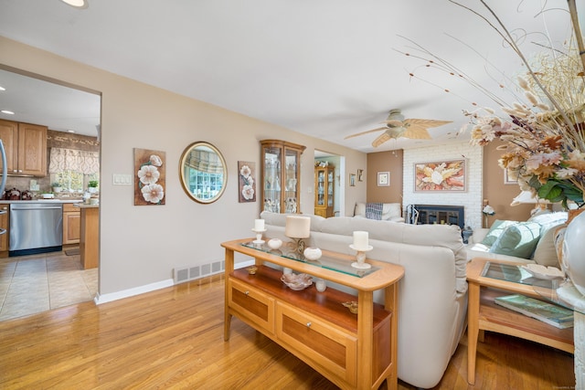living room featuring ceiling fan, visible vents, light wood-style flooring, and a fireplace