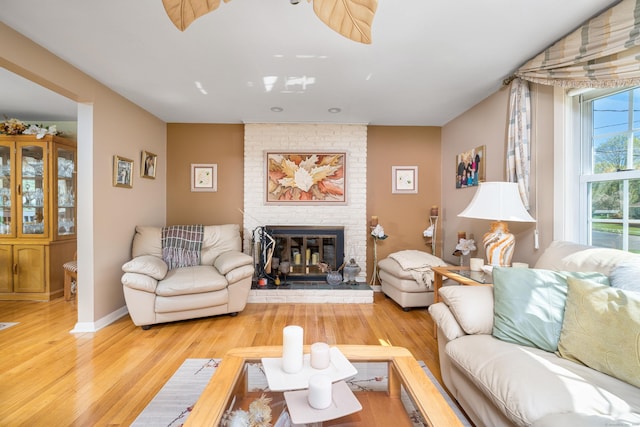 living area with baseboards, a brick fireplace, and light wood-type flooring