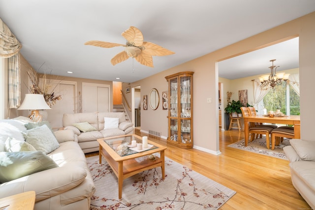 living area with light wood finished floors, ceiling fan with notable chandelier, stairs, baseboards, and visible vents