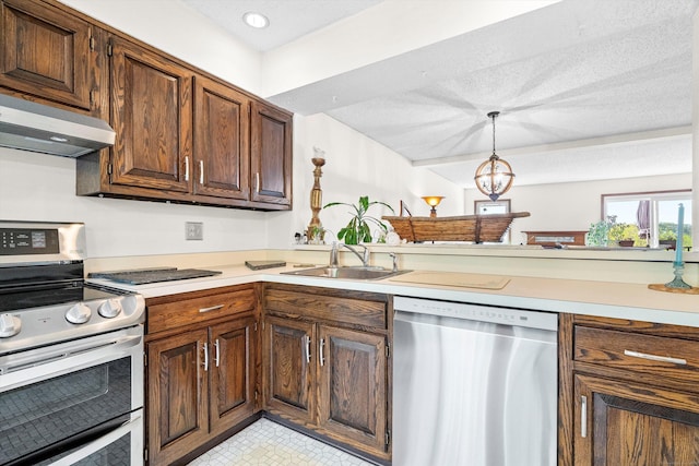 kitchen featuring pendant lighting, light countertops, under cabinet range hood, a sink, and appliances with stainless steel finishes