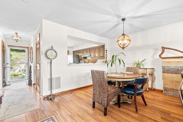 dining room with a textured ceiling, visible vents, baseboards, light wood finished floors, and a chandelier