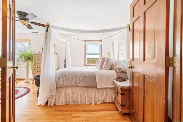 bedroom featuring light wood-type flooring, a textured ceiling, visible vents, and multiple windows