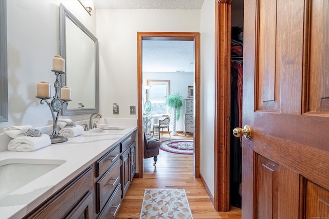 full bathroom with a sink, double vanity, a textured ceiling, and wood finished floors