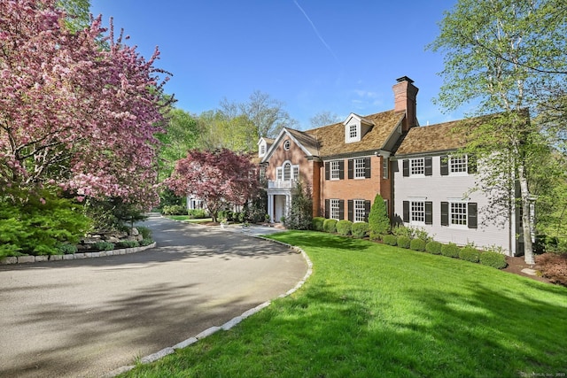 colonial-style house featuring a chimney, a front lawn, and aphalt driveway