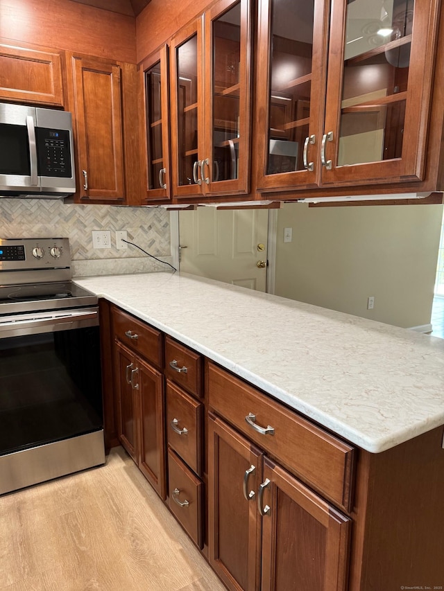 kitchen featuring light countertops, glass insert cabinets, tasteful backsplash, and stainless steel appliances