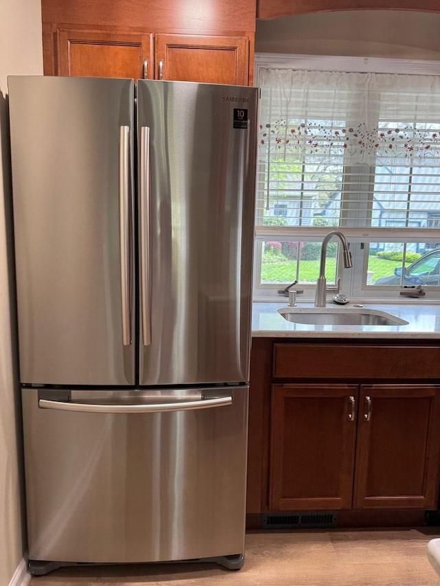 kitchen with brown cabinetry, visible vents, a sink, light countertops, and freestanding refrigerator
