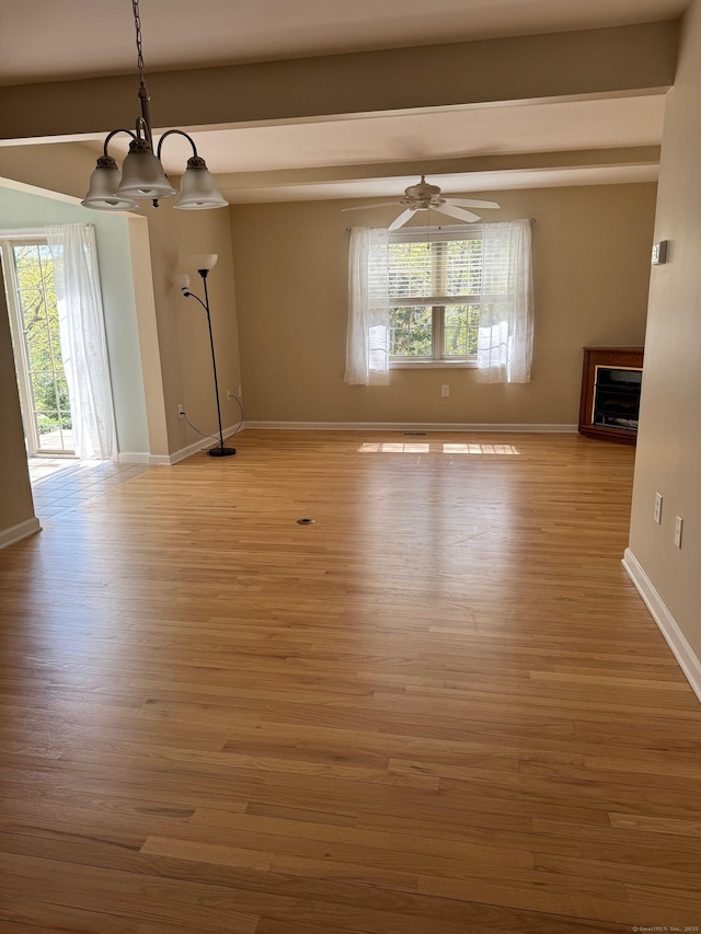 unfurnished dining area with baseboards, ceiling fan with notable chandelier, wood finished floors, and a fireplace