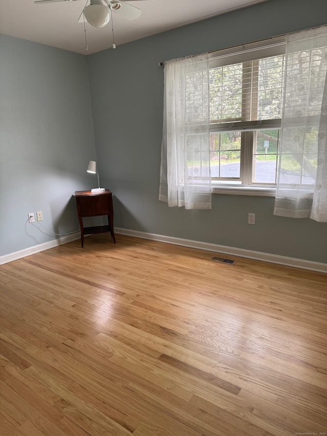 empty room with baseboards, ceiling fan, wood finished floors, and visible vents