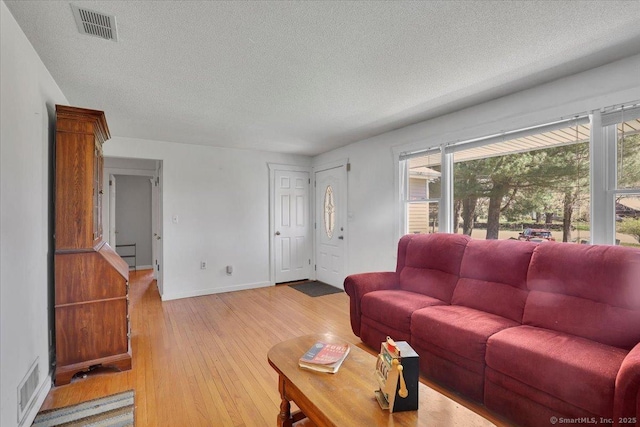 living room with a textured ceiling, visible vents, baseboards, and light wood finished floors
