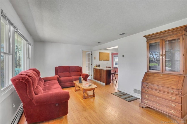 living room with plenty of natural light, a textured ceiling, visible vents, a baseboard radiator, and light wood-style floors
