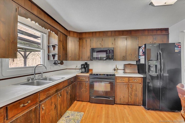 kitchen featuring a textured ceiling, a sink, light countertops, black appliances, and light wood-style floors