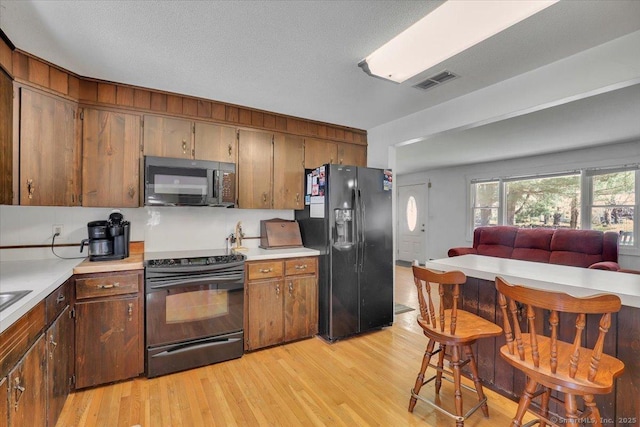 kitchen with light countertops, black appliances, light wood finished floors, and visible vents