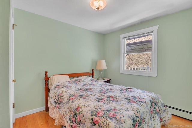 bedroom featuring baseboards, a baseboard heating unit, and wood finished floors