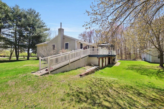rear view of property featuring a lawn, a wooden deck, a chimney, and a gazebo