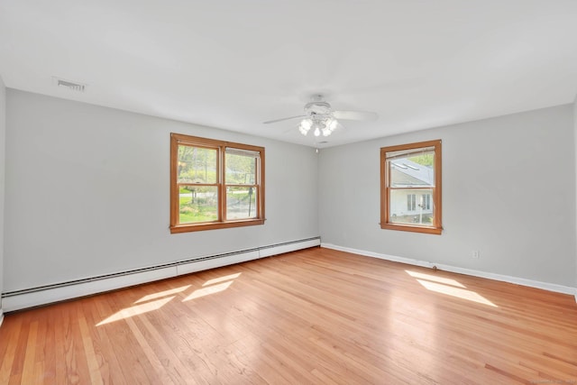 spare room with visible vents, plenty of natural light, a baseboard heating unit, and wood finished floors