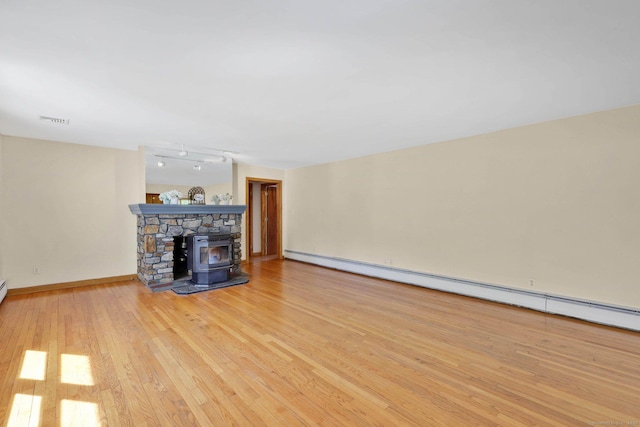 unfurnished living room with visible vents, a wood stove, wood-type flooring, baseboards, and a baseboard heating unit