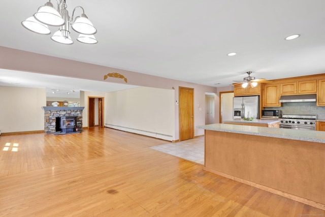 kitchen with appliances with stainless steel finishes, baseboard heating, light wood-style floors, ceiling fan with notable chandelier, and under cabinet range hood