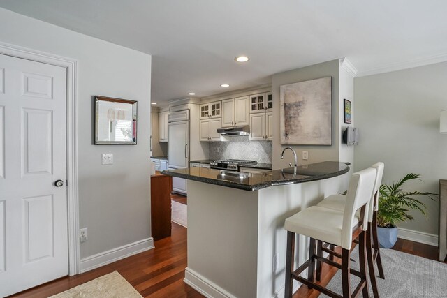 1803 Revere Rd, Danbury, CT 06811 - kitchen with dark wood-style flooring, a kitchen breakfast bar, a peninsula, baseboards, and under cabinet range hood