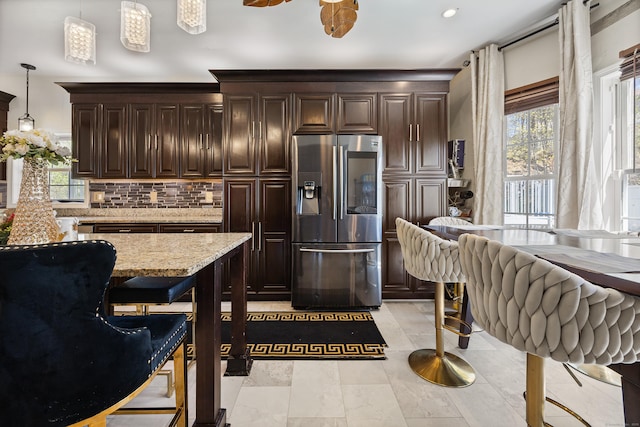 kitchen featuring decorative backsplash, dark brown cabinetry, pendant lighting, light stone counters, and stainless steel fridge