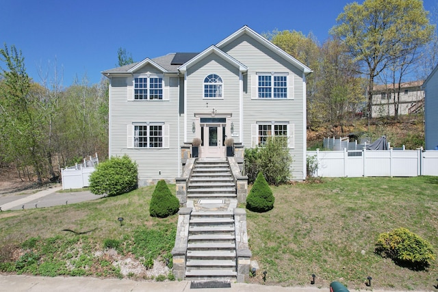 traditional-style house featuring stairway, fence, solar panels, and a front lawn