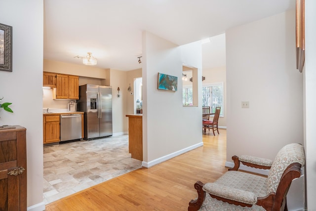 kitchen with appliances with stainless steel finishes, light wood finished floors, light countertops, brown cabinetry, and baseboards