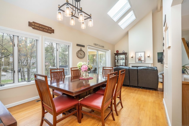 dining space with a skylight, baseboards, high vaulted ceiling, and light wood-type flooring