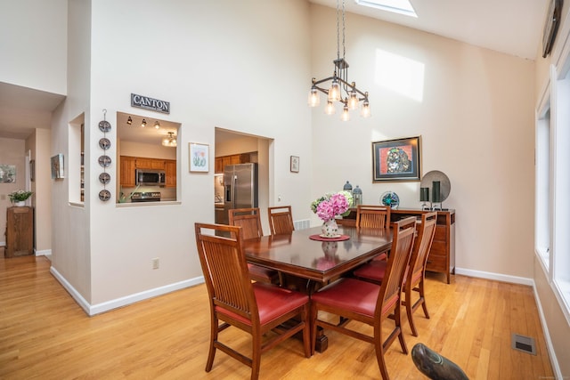 dining room with light wood-style floors, baseboards, a towering ceiling, and visible vents
